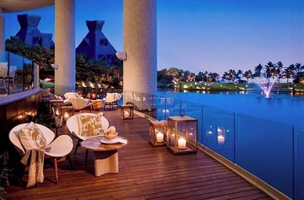 A rooftop lounge with seating, a pool, and a view of palm trees.