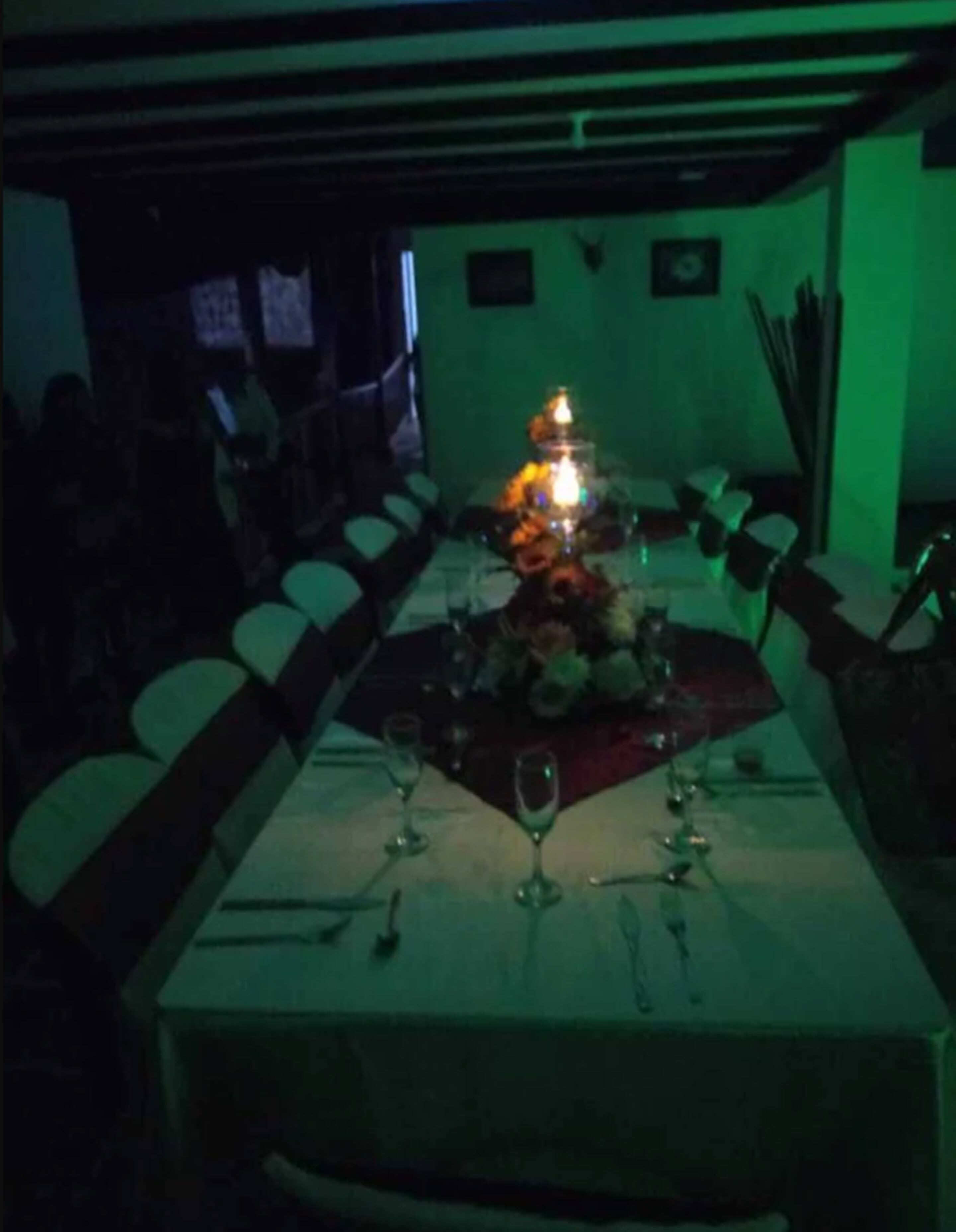 A dimly lit restaurant with a long table set for dining, featuring a central candle and wine glasses.