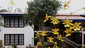 A two-story building with a tiled roof, a stone staircase, and a garden with yellow flowers. - Casa Rayma Hotel Boutique (Contratación)