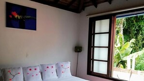 A bedroom with a wooden ceiling, a bed with white bedding and decorative pillows, a window with a view of greenery, and a wall-mounted artwork. - Casa Rayma Hotel Boutique (Contratación)
