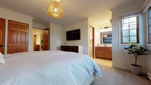 Ein Schlafzimmer mit einem großen Bett, einem Fernseher, einem Badezimmer mit Waschbecken und Spiegel sowie einer Topfpflanze.