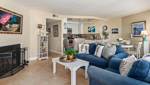 A living room with a fireplace, a blue sofa set, a coffee table with a plant, and a bookshelf.