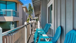 A balcony with blue chairs, a railing, and a view of adjacent buildings.