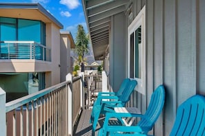 A balcony with blue chairs, a railing, and a view of adjacent buildings.