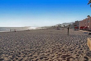 A beach with a clear sky, people walking, and buildings in the background.