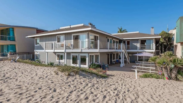 A beachfront property with a two-story building, a covered patio, and a sandy beach.