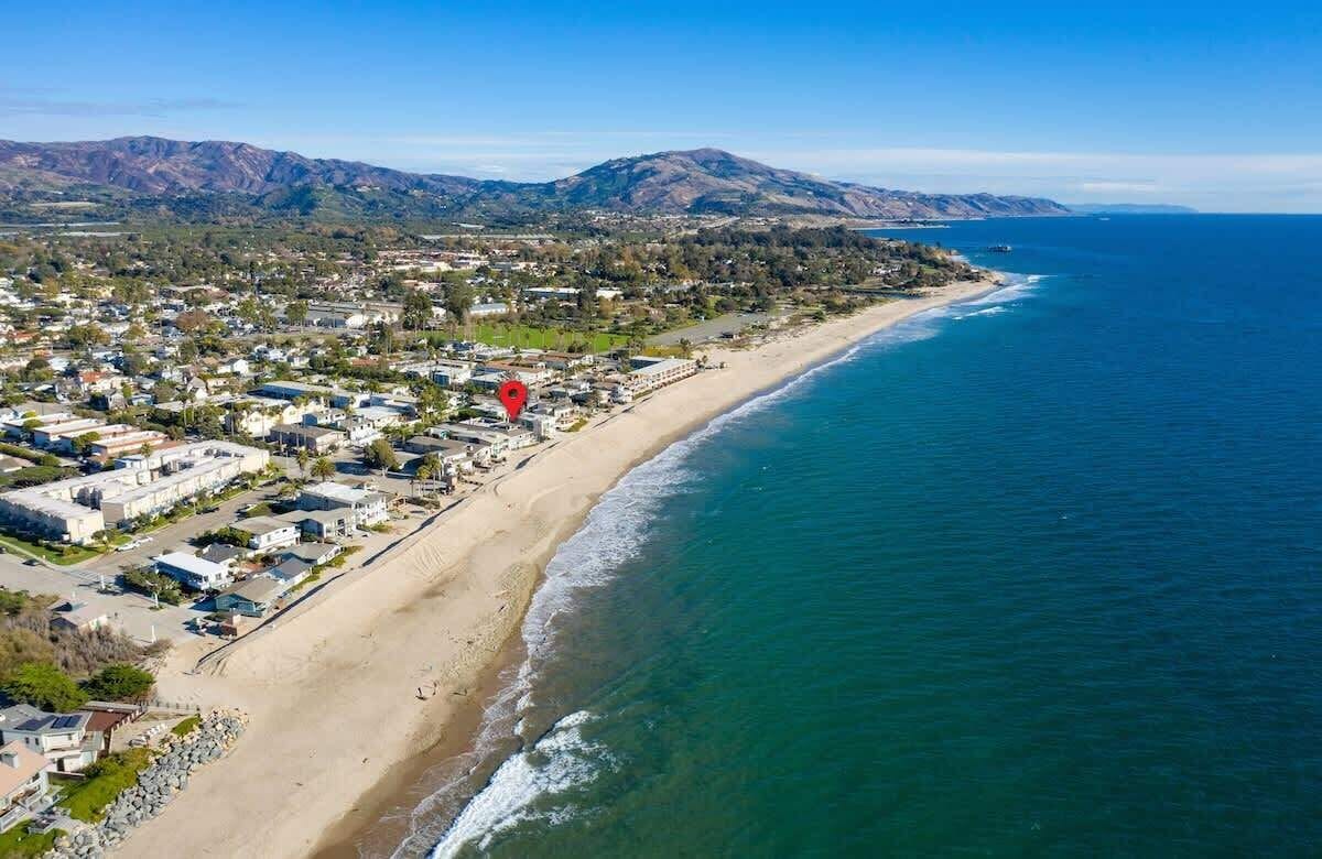An aerial view of a coastal town with a beach, houses, and mountains in the background.