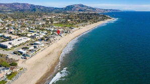 An aerial view of a coastal town with a beach, houses, and mountains in the background.