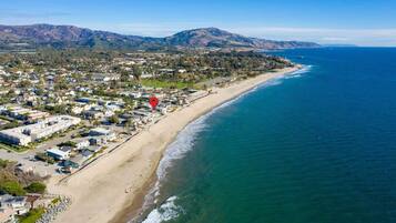 An aerial view of a coastal town with a beach, houses, and mountains in the background.