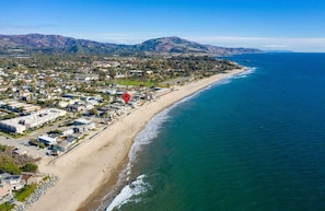 An aerial view of a coastal town with a beach, houses, and mountains in the background.