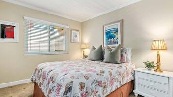 A bedroom with a bed, two bedside lamps, a nightstand, a framed picture, and a window with blinds.