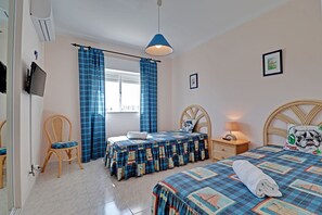 A bedroom with two beds, a chair, a nightstand, a lamp, and a television.