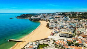 An aerial view of a coastal town with a sandy beach, a pier, and densely packed buildings with varied architecture.