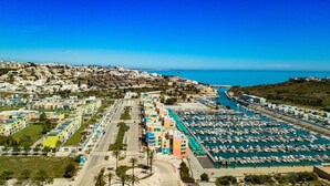 Un poble costaner amb edificis de colors, una marina plena de vaixells i un cel blau i clar.