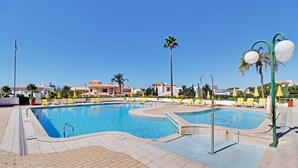 Una piscina amb gandules i ombrelles, envoltada per palmeres i edificis.