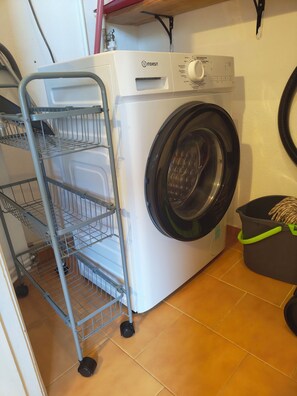 Eine Waschmaschine mit Frontlader und ein Metallregal daneben.