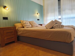 Ein ordentlich bezogenes Bett mit einer gestreiften Tagesdecke, zwei Zierkissen und zusammengerollten Handtüchern auf einem Nachttisch aus Holz.