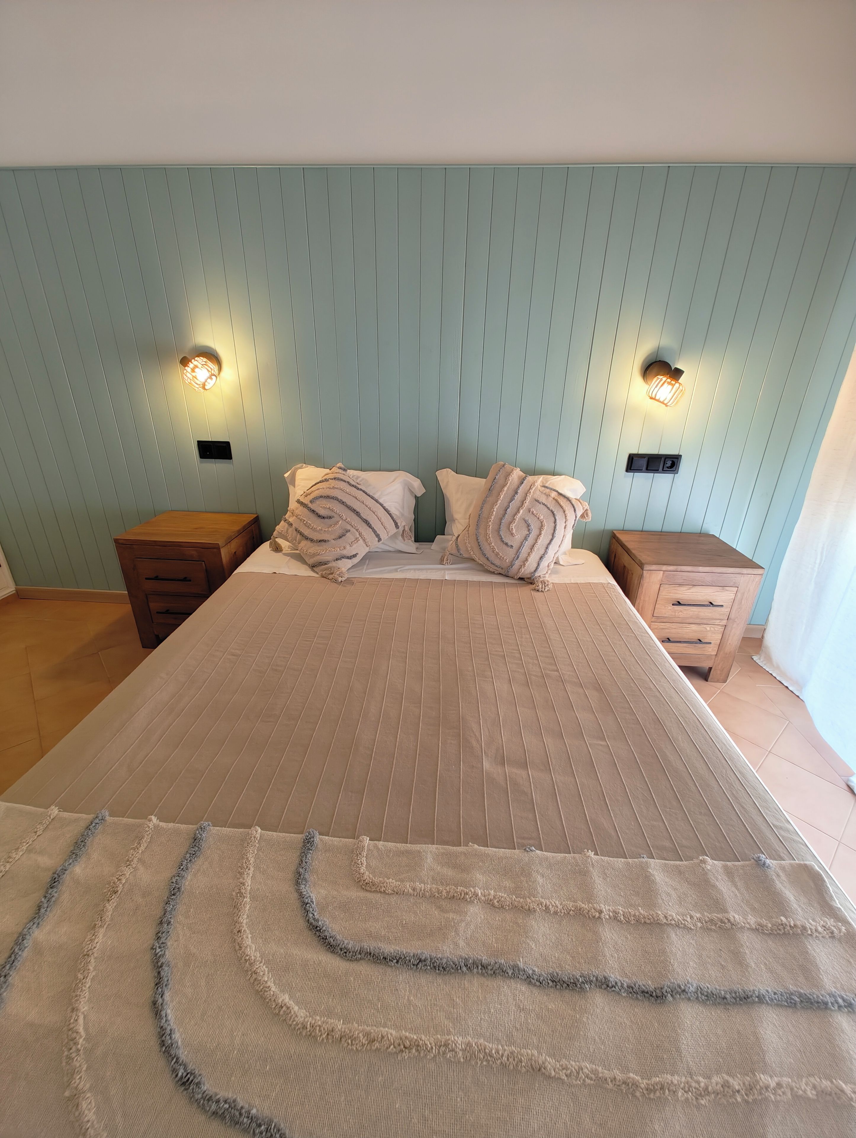 Une chambre à coucher avec un lit, deux tables de chevet et des lampes fixées au mur.