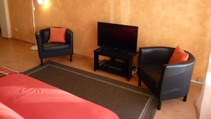 A room with a bed, two armchairs, a TV on a stand, and a floor lamp. - Apartment, with pool, near the beach (Albufeira)