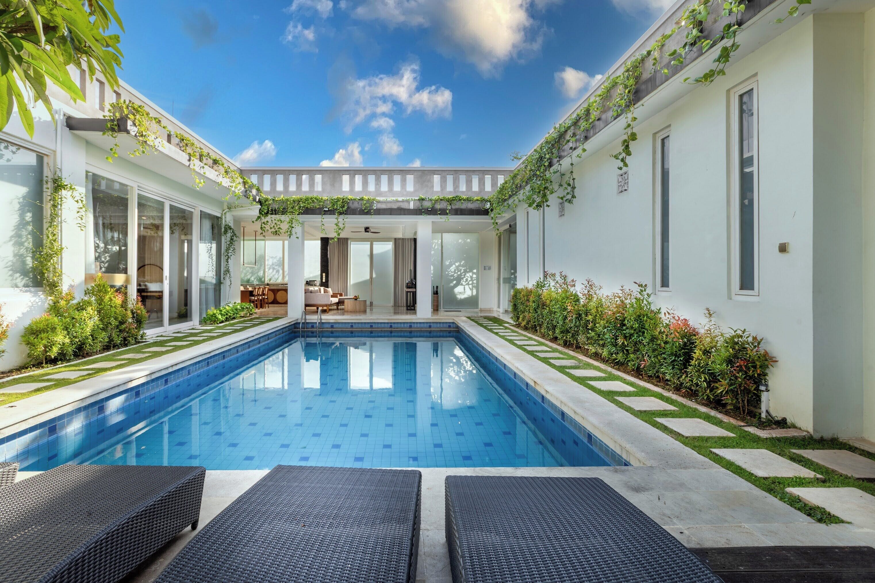 Un área de piscina moderna con una piscina azul cristalina, rodeada de paredes blancas y plantas verdes.