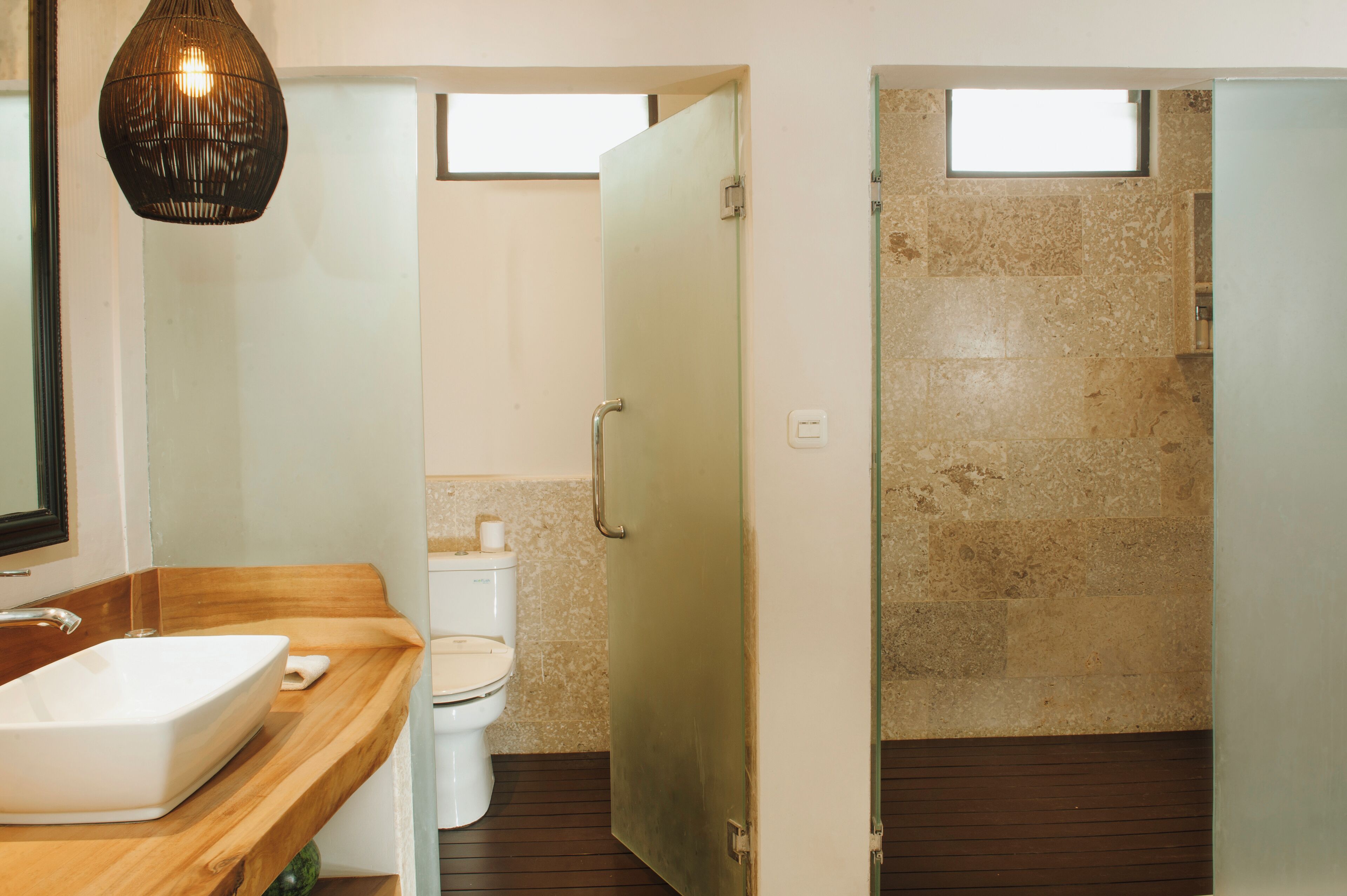 A modern bathroom with a wooden vanity, a white sink, a toilet, and a glass shower door.