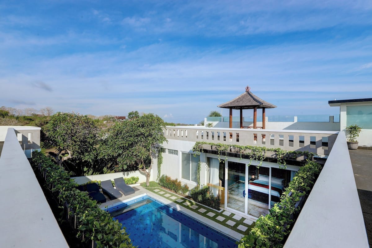 A modern pool area with a glass-enclosed pool, lounge chairs, and a gazebo.