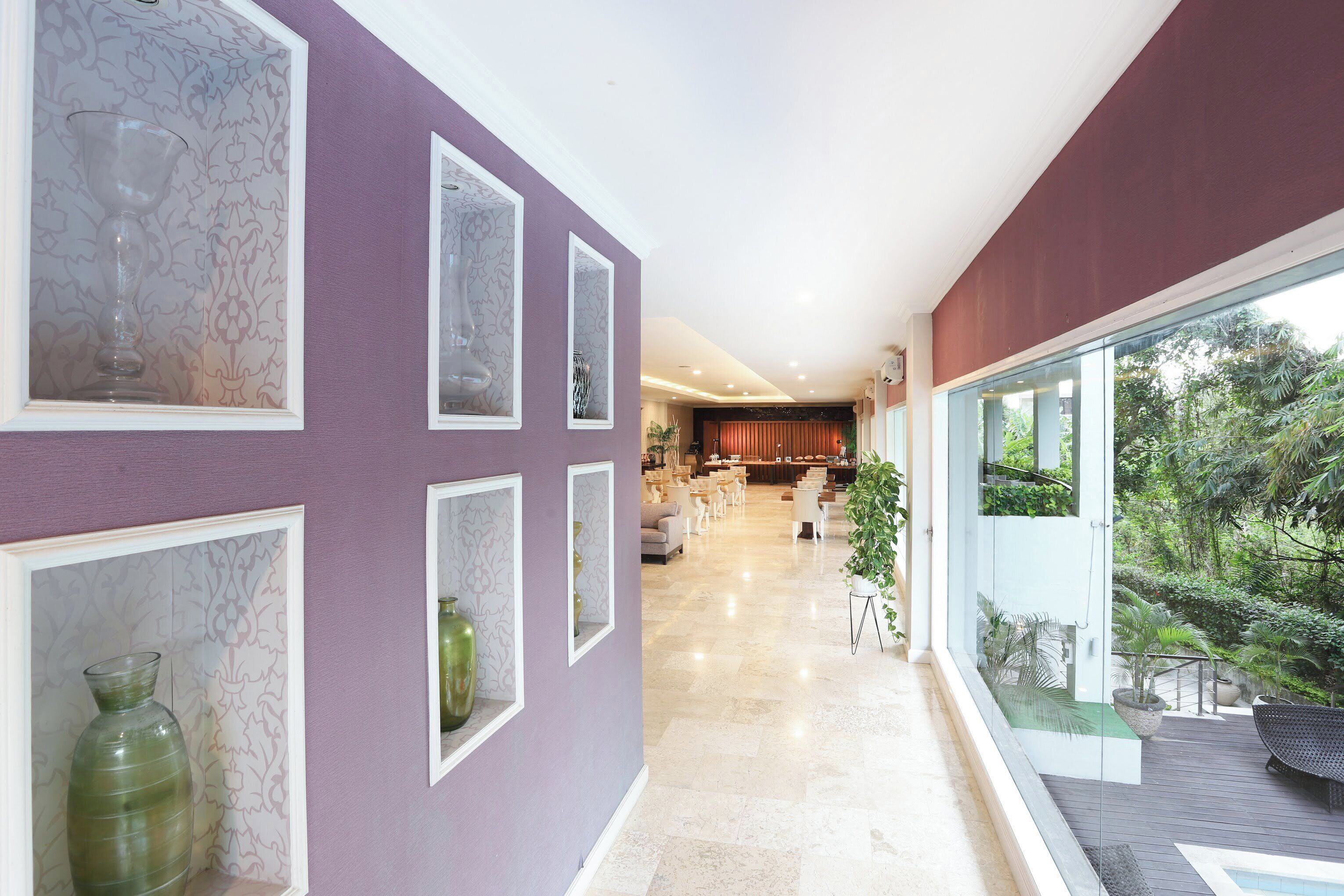 A modern interior with a purple wall, framed artwork, and a view of a dining area.