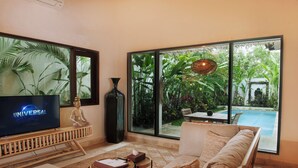 Sala de estar con televisor, sofá, mesa de centro y vista a una piscina y jardín.