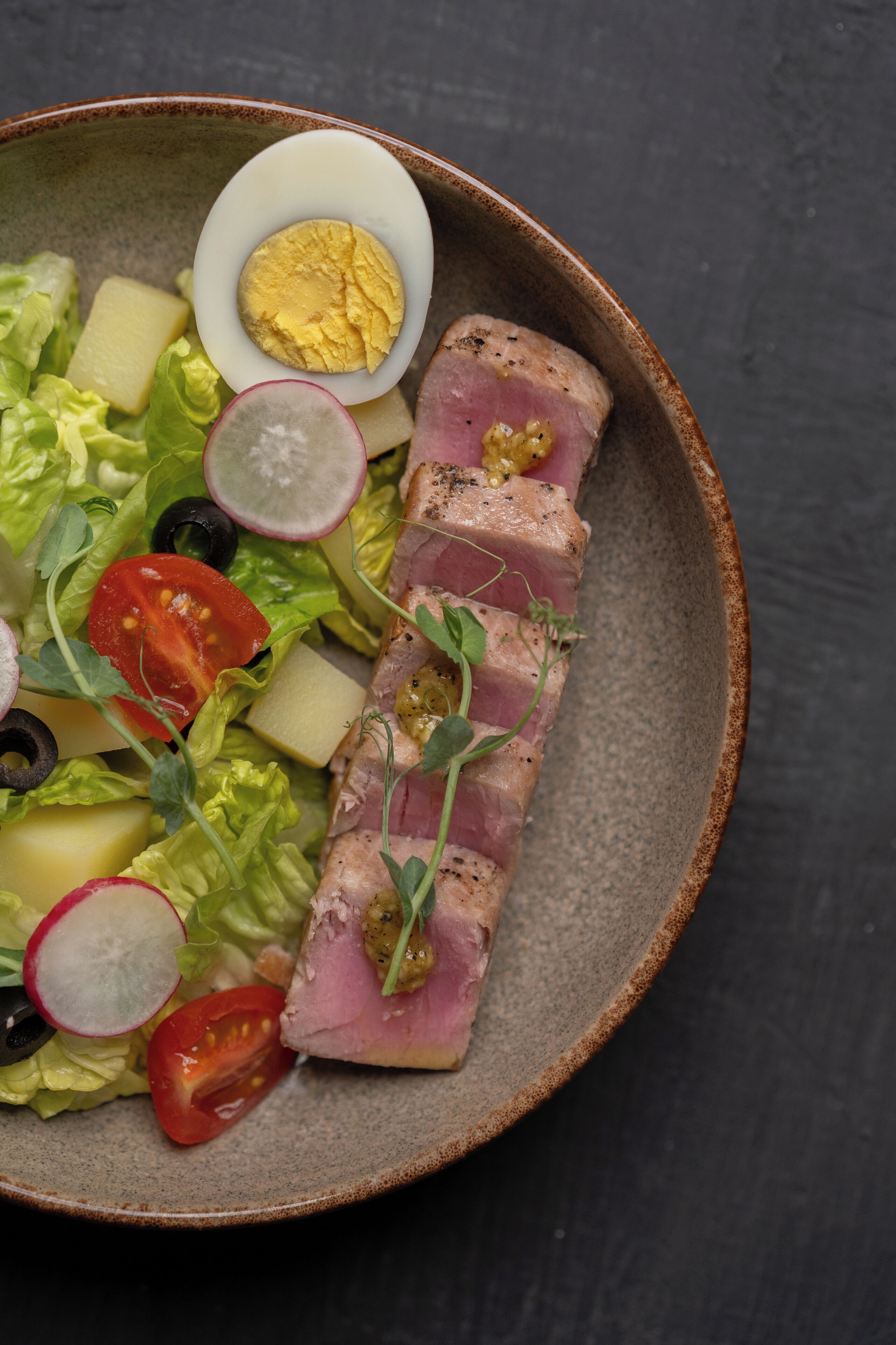 A bowl of food with various ingredients including lettuce, tomatoes, radishes, and a boiled egg.