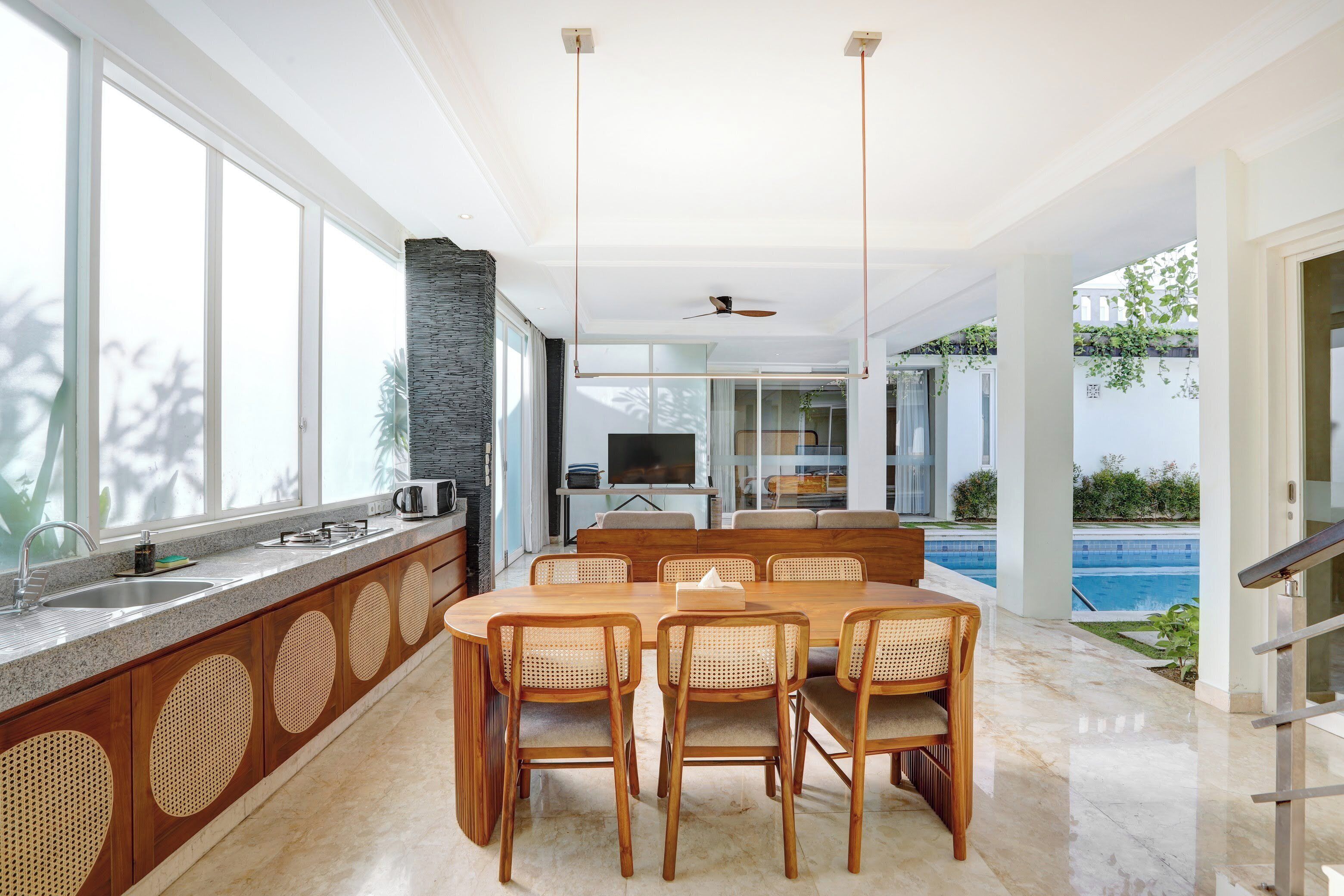 A modern kitchen with a dining area, large windows, and a view of a swimming pool.