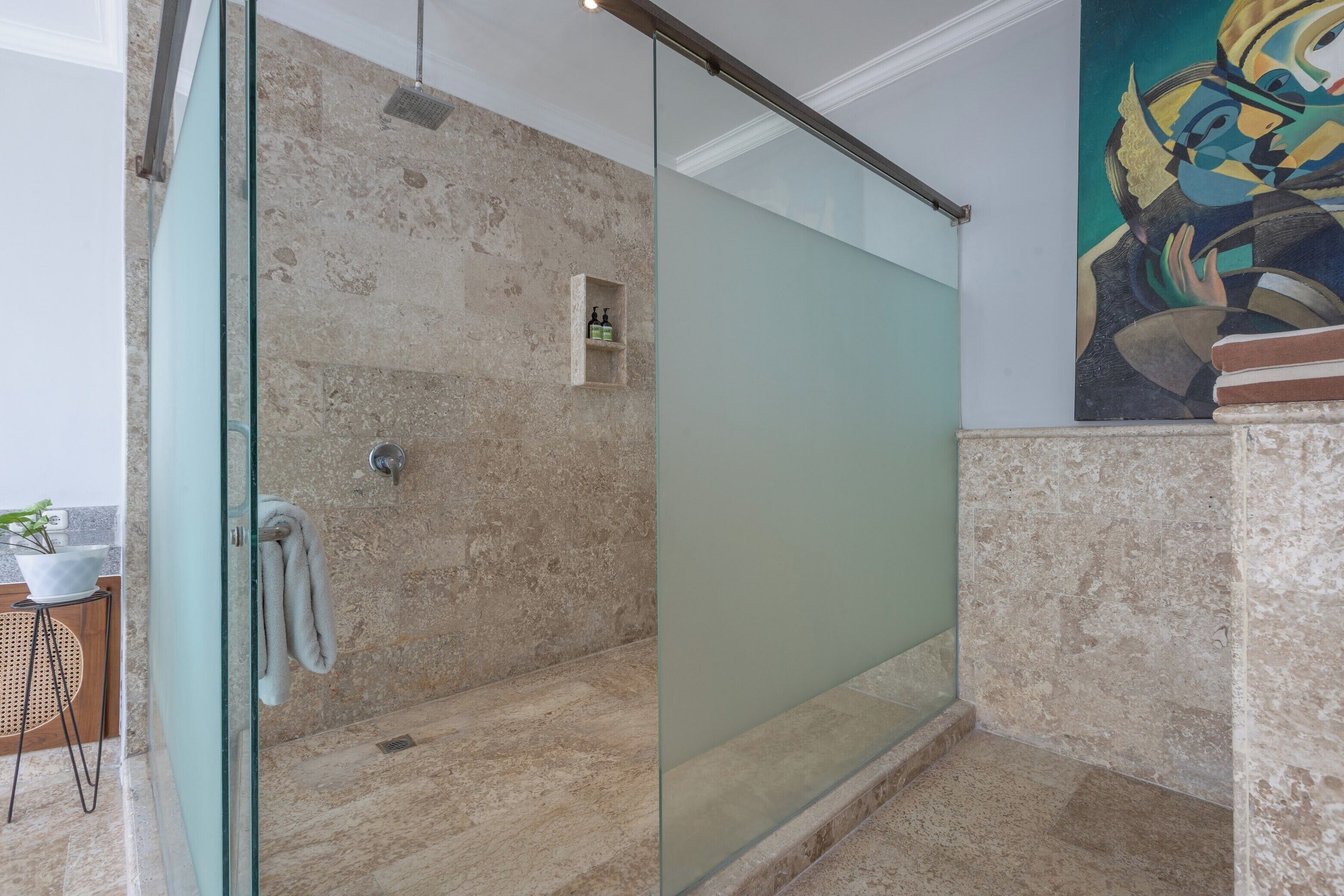 A modern bathroom with a glass shower enclosure, marble walls, and a small shelf with toiletries.