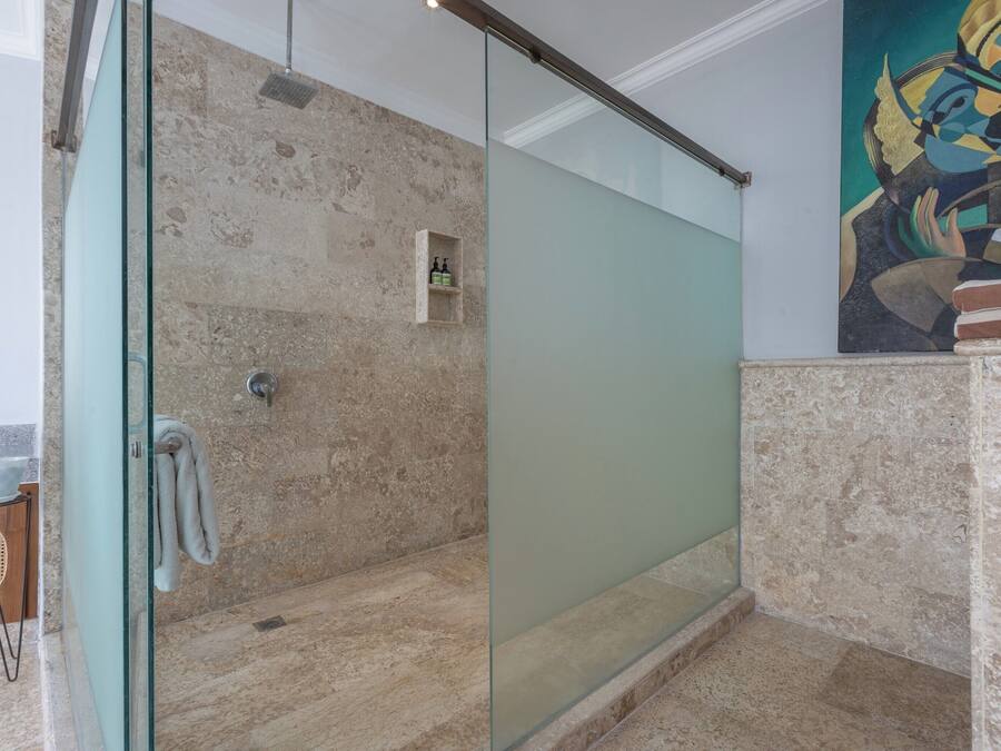 Un baño moderno con cabina de ducha de vidrio, paredes de mármol y un pequeño estante con artículos de aseo.