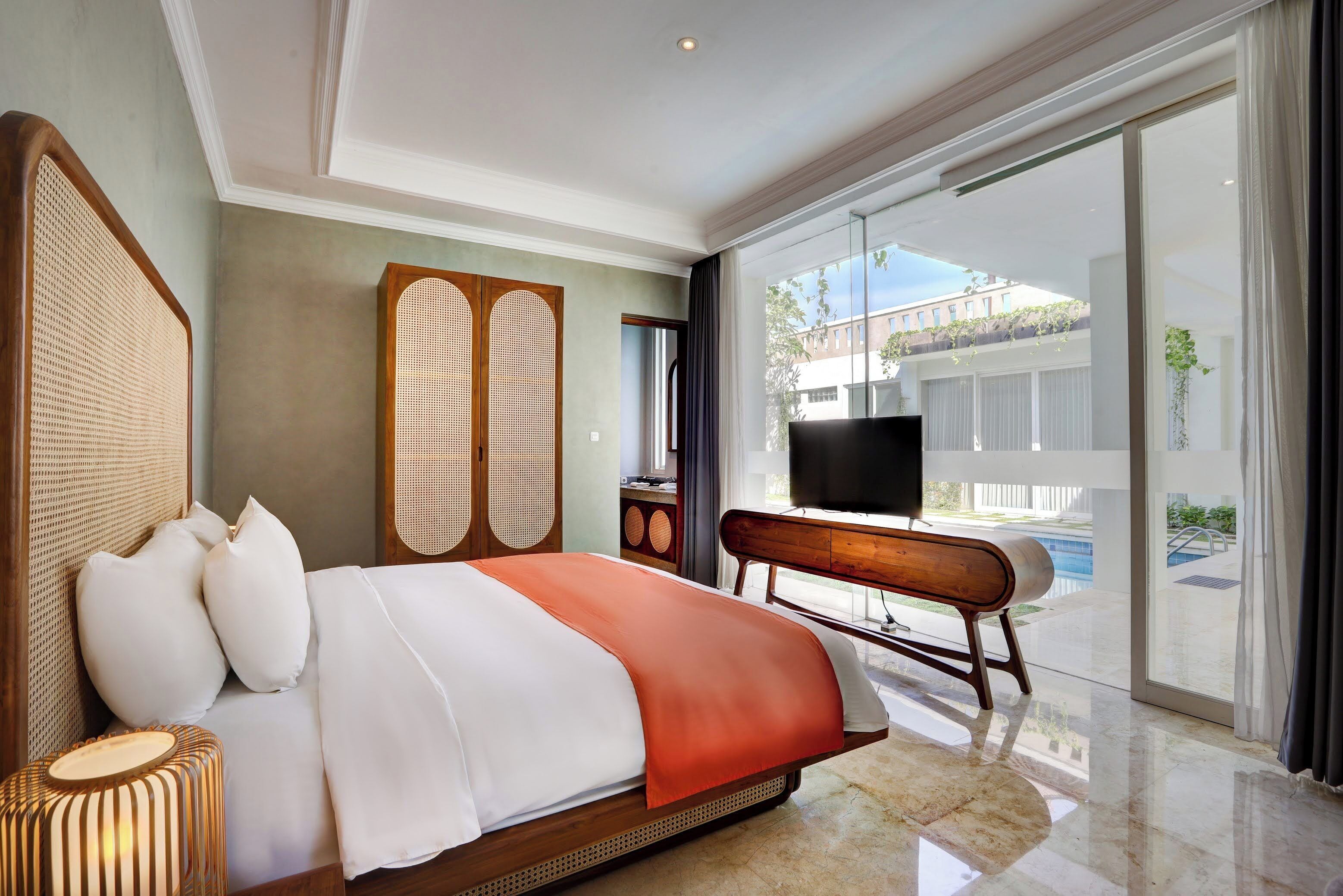 A modern hotel room with a large bed, a TV, a desk, and a view of the outdoor swimming pool.