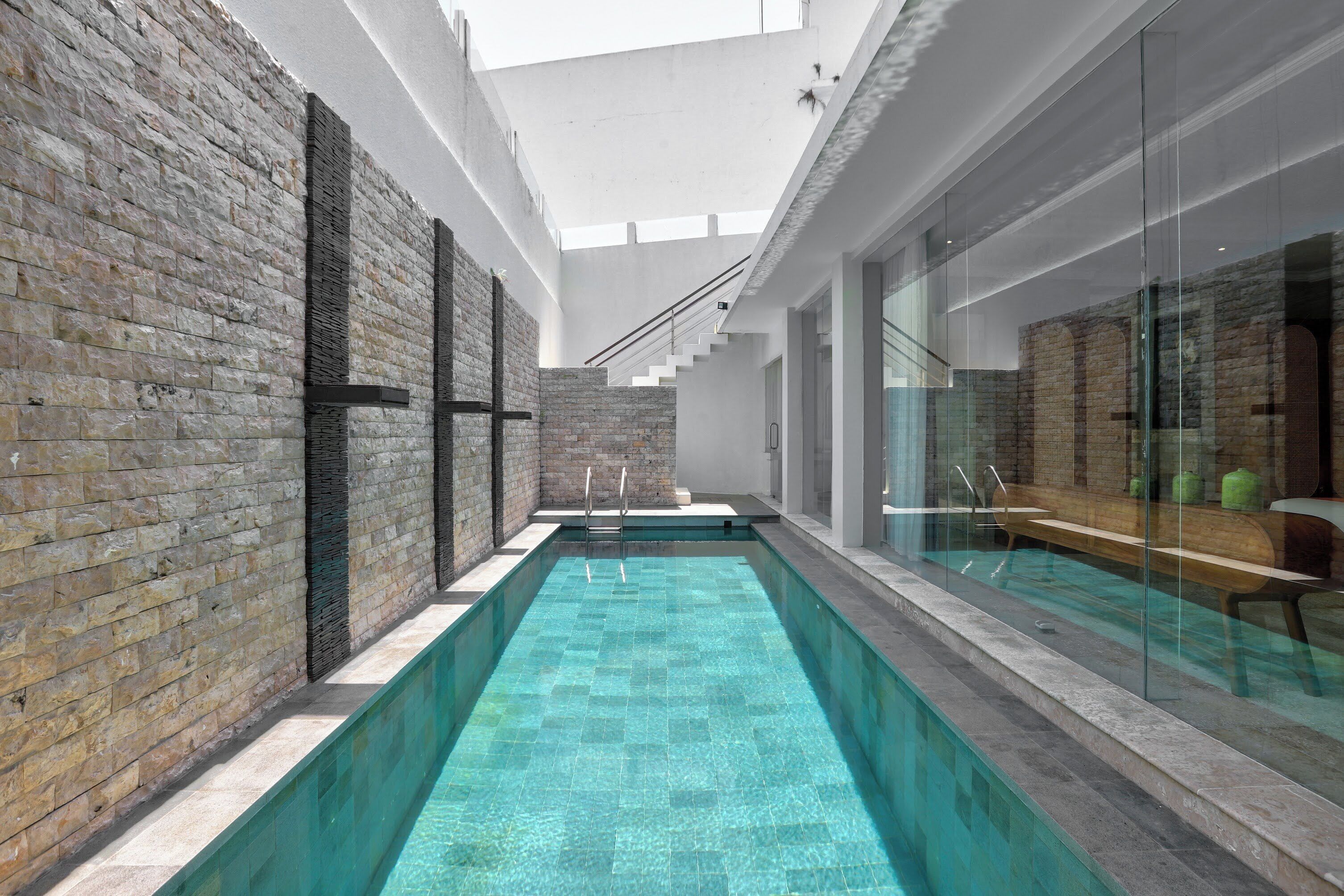 A modern indoor pool with clear blue water, surrounded by stone walls and glass panels.