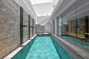 A modern indoor pool with clear blue water, surrounded by stone walls and glass panels.