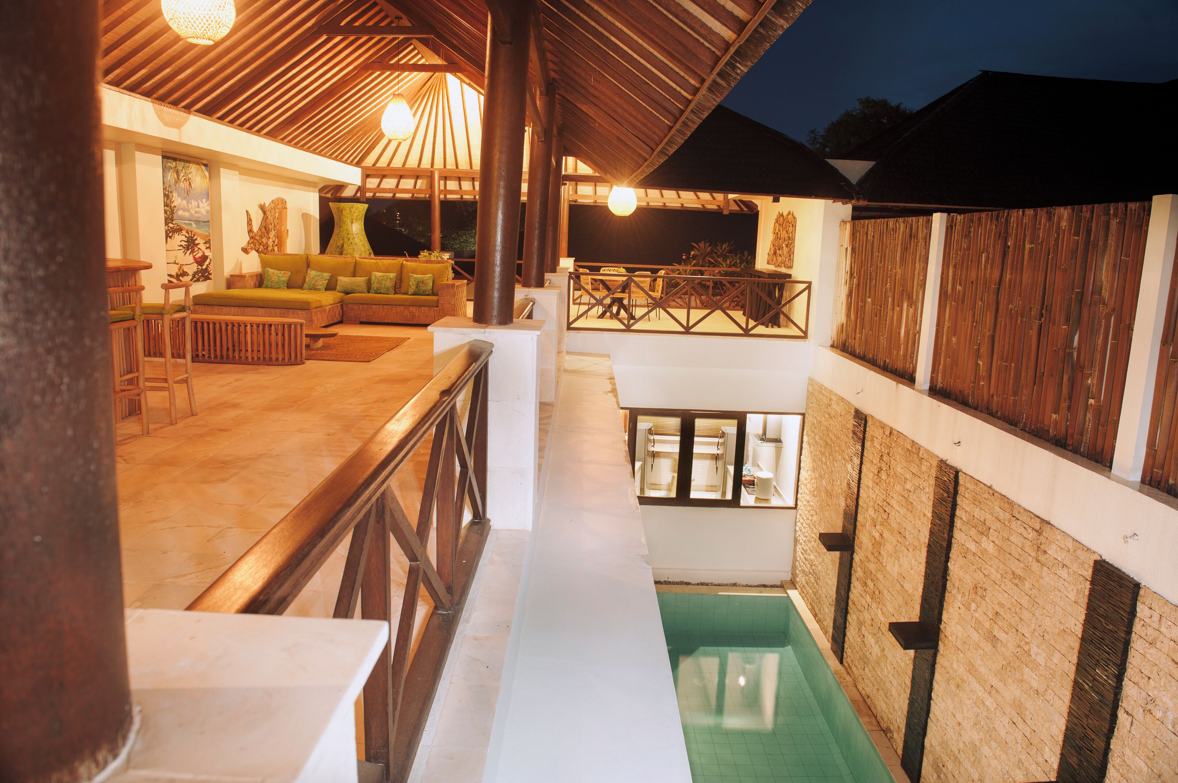 A rooftop pool area with a wooden deck, seating, and a view of the night sky.