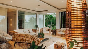 Un salón moderno con mobiliario de mimbre, ventanas amplias y una lámpara decorativa.