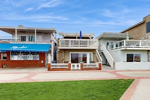 A beachfront property with a blue awning, a balcony with a white railing, and a stone facade.
