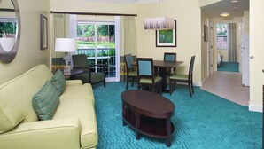 Une chambre d’hôtel équipée d’un canapé, d’une table à manger avec des chaises, d’une télévision et offrant une vue sur un jardin grâce à une porte coulissante.