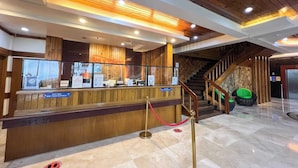 A reception area with a wooden counter, a staircase, and a glass display case. - Sol Y Viento Hotel and Resort (Calamba)