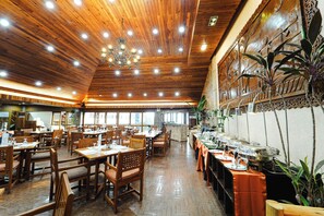 A spacious restaurant with wooden ceiling and walls, featuring a long counter with food service stations and several tables with chairs. - Sol Y Viento Hotel and Resort (Calamba)
