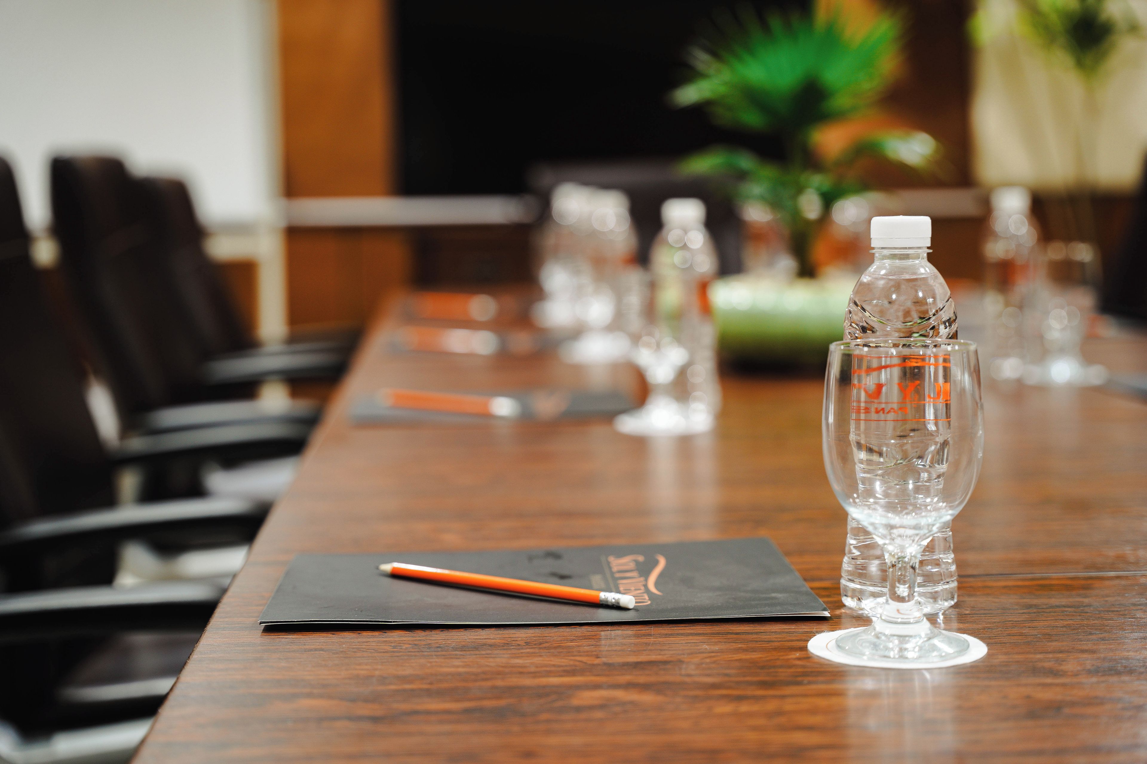 Une table de conférence avec une bouteille d’eau, un verre et un crayon posés sur un set de table noir.