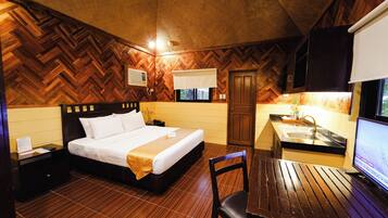 A hotel room with a wooden herringbone floor, a bed with white linens, a wooden desk with a chair, a sink, and a television.
