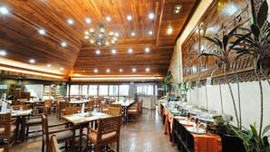 A spacious restaurant with wooden ceiling and walls, featuring a long counter with food service stations and several tables with chairs. - Sol Y Viento Hotel and Resort (Calamba)