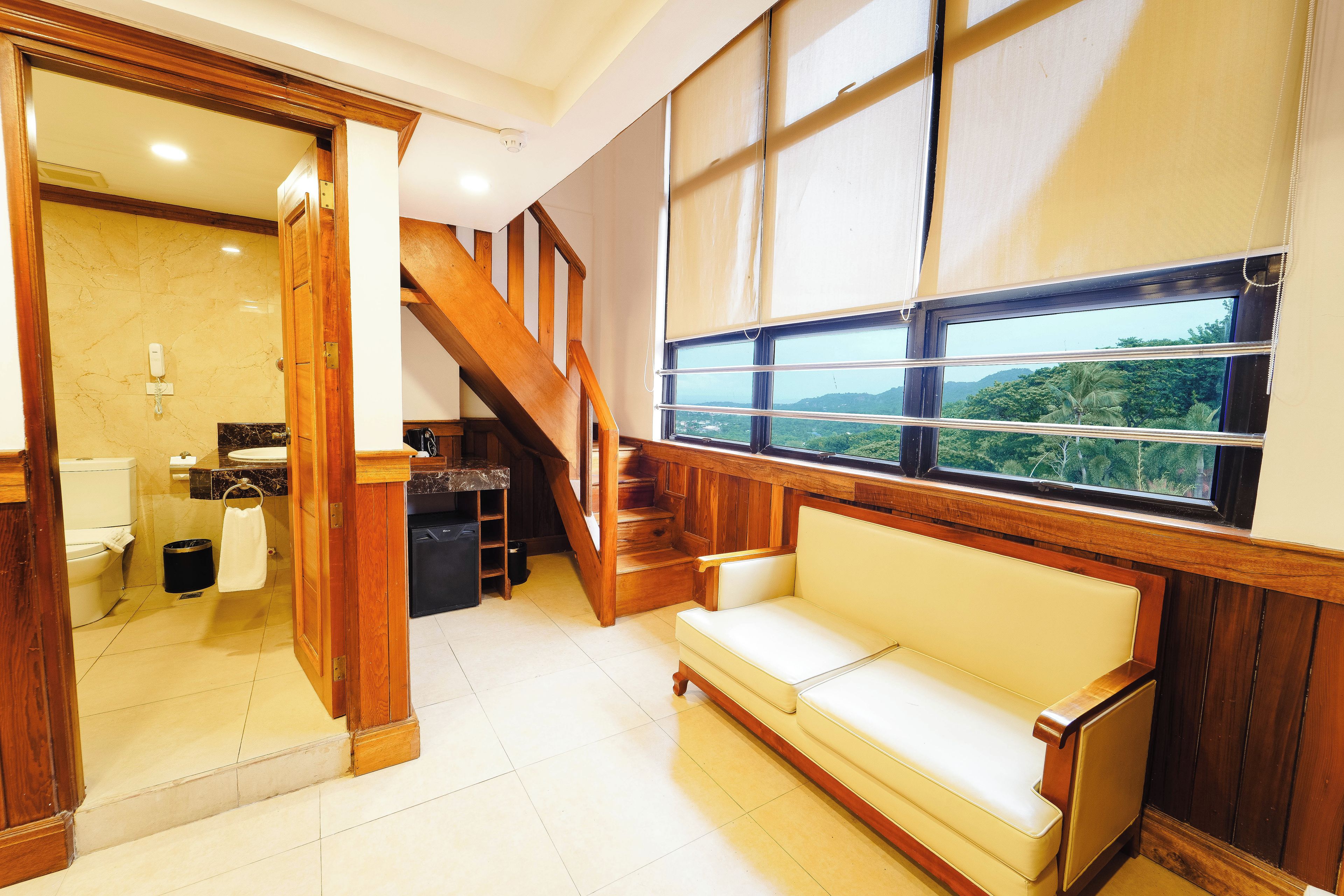 Uma sala de estar espaçosa com escada de madeira, um sofá bege e uma janela ampla com vista para o verde.