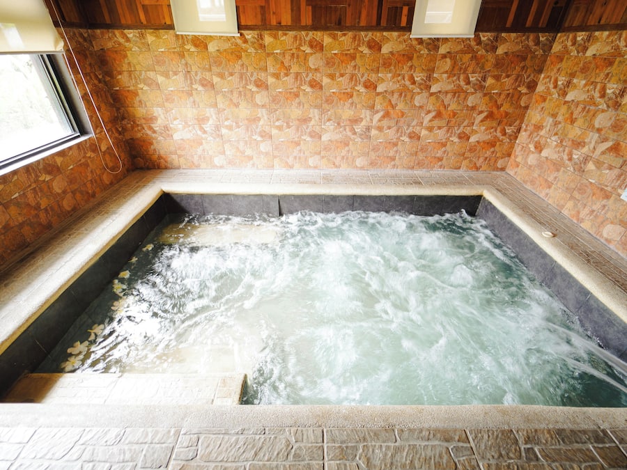 Uma banheira de hidromassagem com água corrente, rodeada por azulejos de pedra e painéis de madeira.