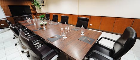 A conference room with a long wooden table, black leather chairs, and a large flat-screen TV.