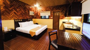 A hotel room with a wooden herringbone floor, a bed with white linens, a wooden desk with a chair, a sink, and a television. - Sol Y Viento Hotel and Resort (Calamba)