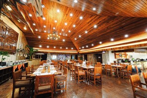 A spacious restaurant with wooden flooring and ceiling, multiple dining tables and chairs, and a kitchen area visible in the background. - Sol Y Viento Hotel and Resort (Calamba)