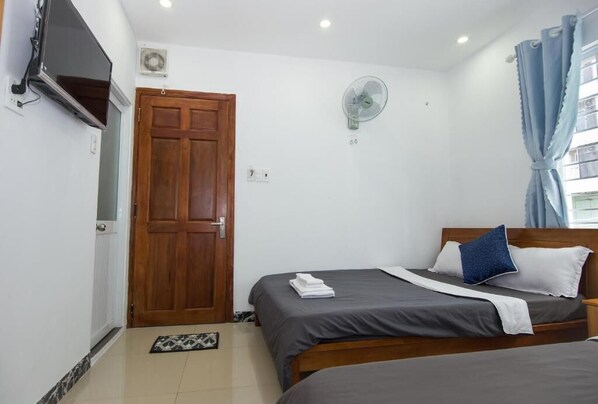Un dormitorio con dos camas, un televisor montado en la pared, un ventilador de techo y una puerta de madera.